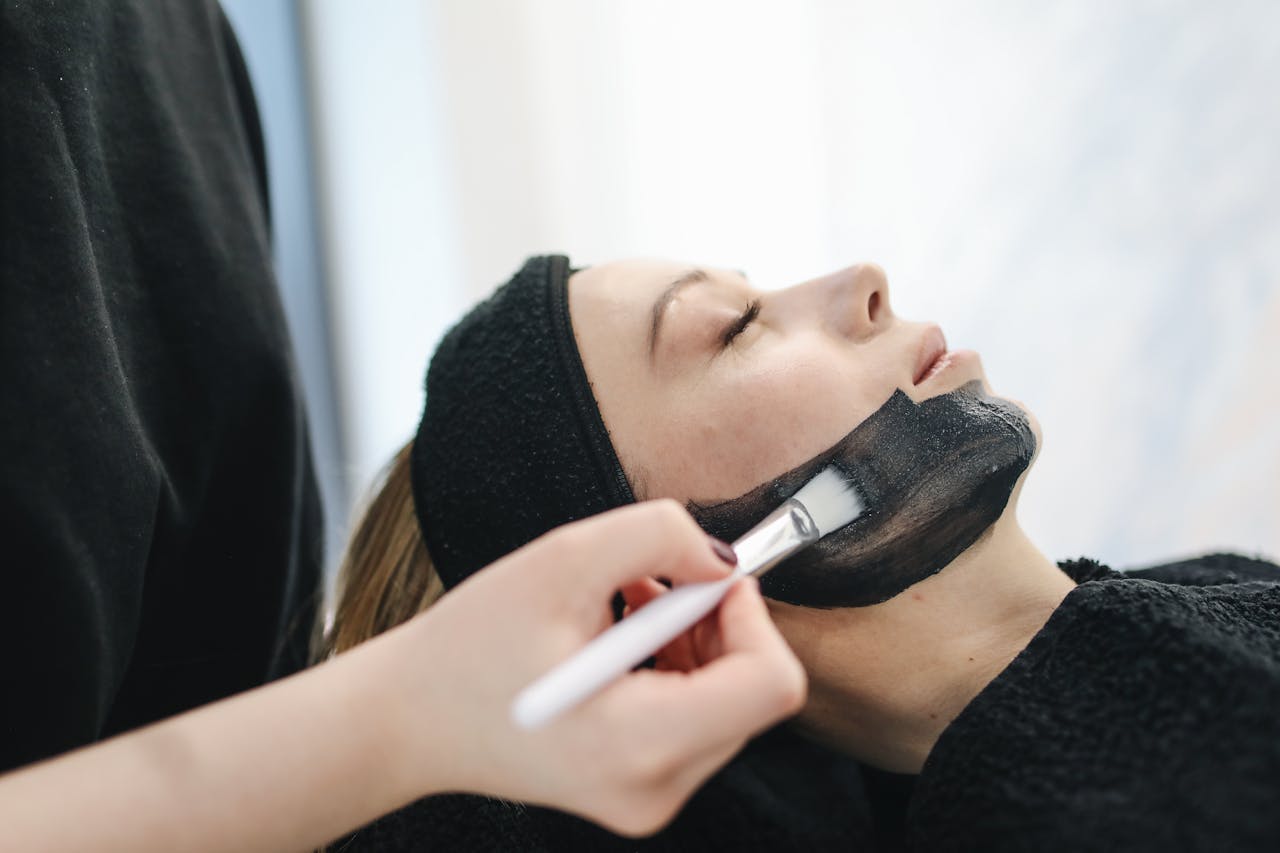 Close-up of a woman enjoying a relaxing charcoal facial treatment in a spa.